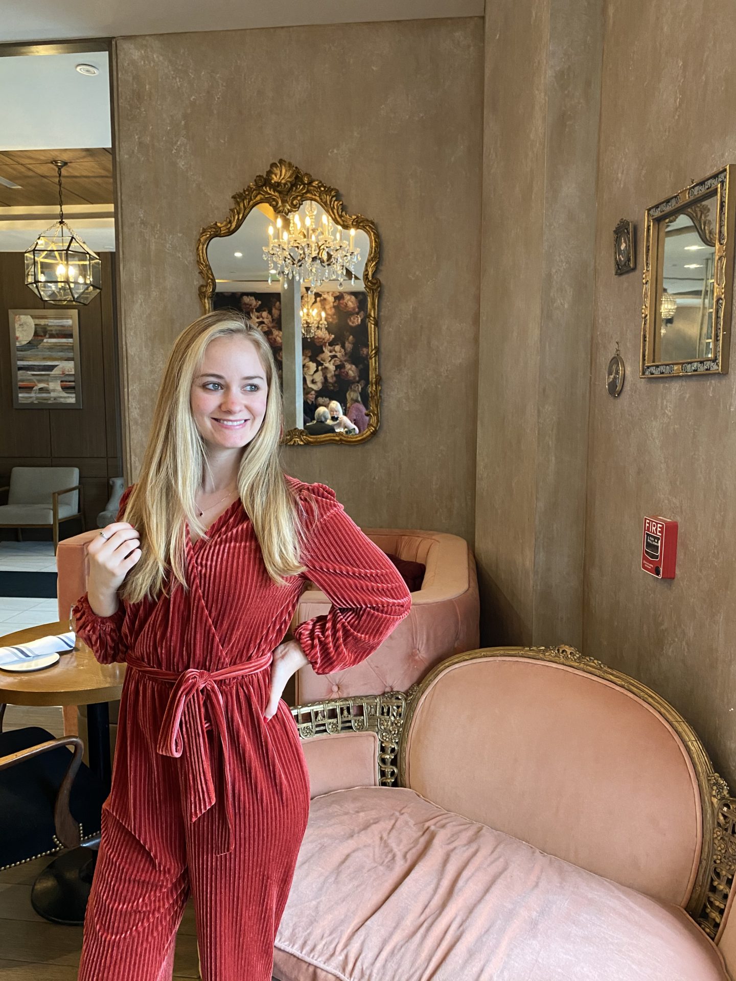 blonde girl in red jumpsuit in front of pink couch