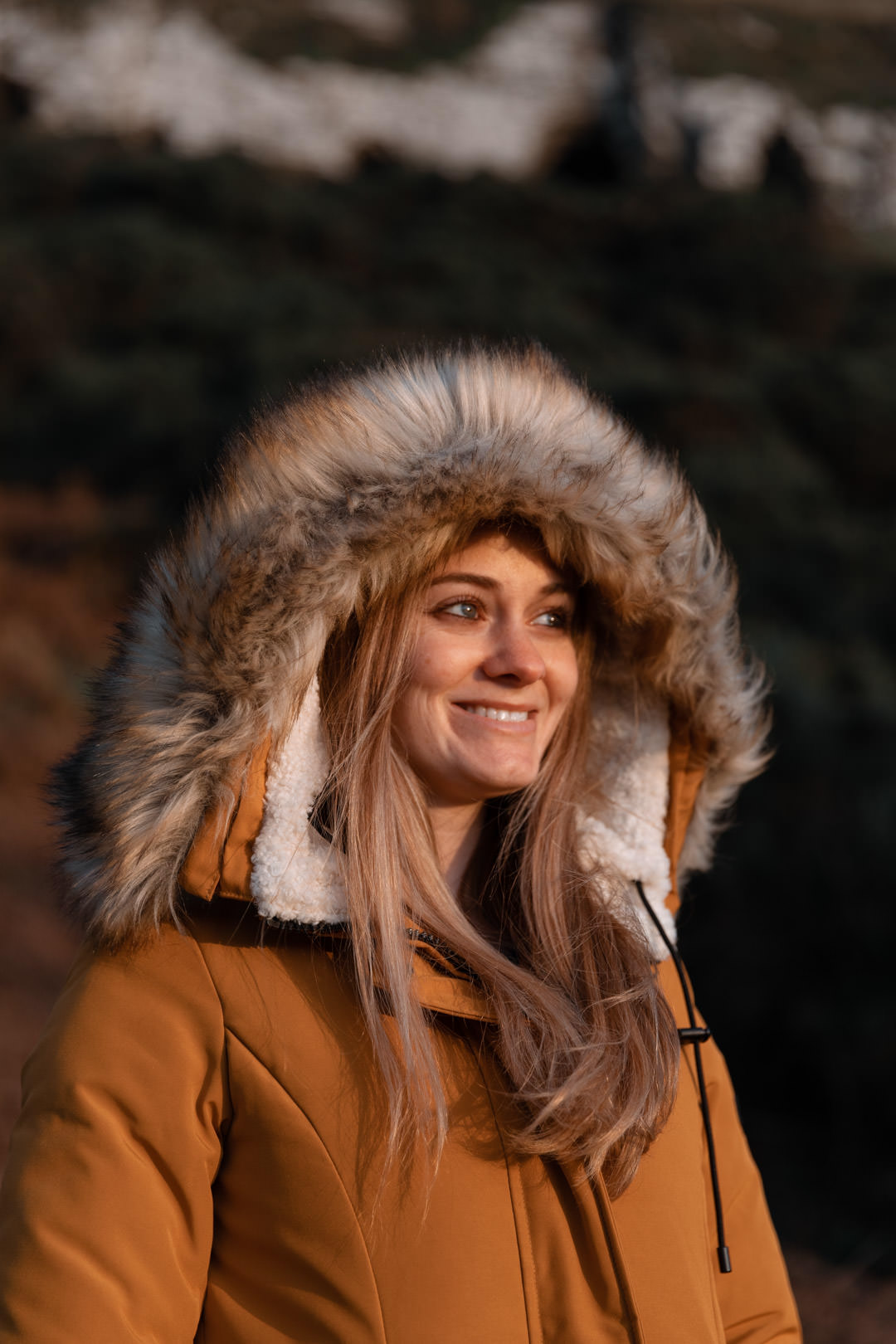 girl in winter coat looking at sun at golden hour